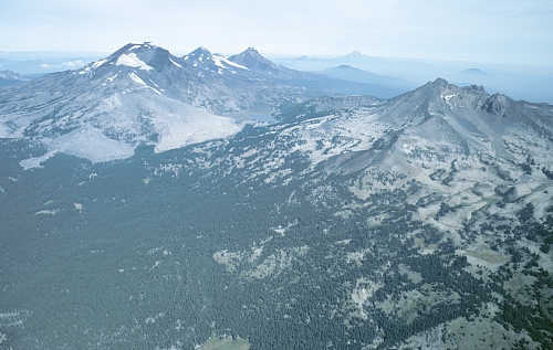 [Aerial view from southeast of Three Sisters volcanic center (South, Middle, and North Sister left of center; Broken Top right of center). Light colored areas on south flank of South Sister are 2,000-yr-old lava flows. Much of area on lower flanks of Broken Top is mantled by pumice and ash erupted just prior to emplacement of these lava flows. Photo by William E. Scott, USGS.] 