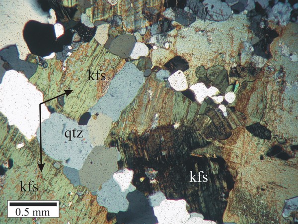 Arrows point to an optically continuous K-feldspar grain separated by quartz-filled fractures in orthogneiss.  K-feldspar is stained green in this image, and sodic perthite appears orange.