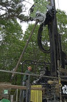 Photograph shows the drill head positioning a new section of drill casing.