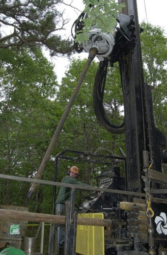Photograph shows the drill head positiong a new section of drill casing.