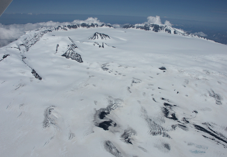 Aerial view of Veniaminof Volcano looking north-northeast across the ice-filled,   8 x 11 km (5 x 7 mi) wide summit caldera. The active intracaldera cone is in the upper left.