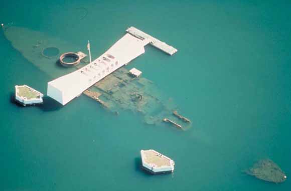 Photograph taken from the air showing the sunken battleship Arizona under shallow water and the memorial structure over it