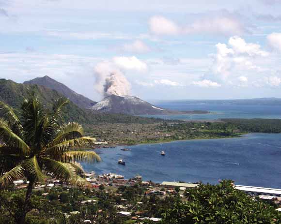 photo of volcano erupting along coast with village in the foreground