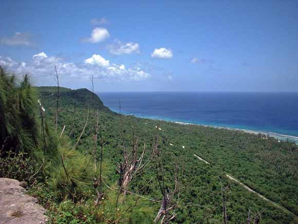 Photograph of coastline with tropical vegetation on the hills in the foreground and the ocean in the background