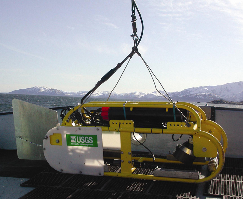 USGS video sled aboard the R/V Alaskan Gyre in Glacier Bay (April 2004). The sled is equipped with forward- and downward-looking video cameras, lights, altimeter, pressure sensor, and pitch and roll sensors. Two down-pointing lasers spaced 20 cm apart provide scale on the seafloor. Position is tracked using ship navigation and an estimate of sled layback.