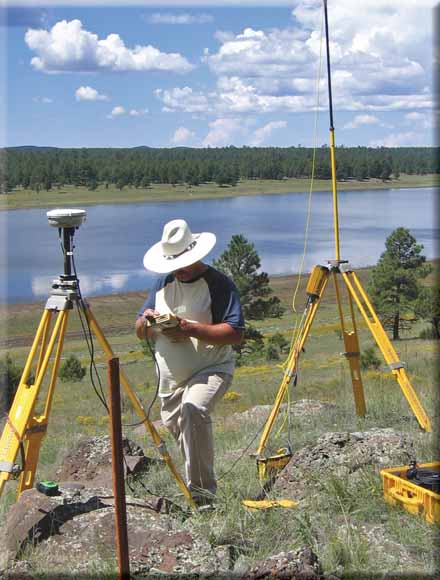 Photo of worker with tripod-mounted GPS equipment and a lake in the background