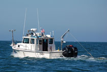 A photograph of the R/V Rafael showing the configuration of acquisition equipment. The Ashtech antenna and the swath interferometric sonar head are located off the bow, and the Klein 3000 and the Edgetech 424 are deployed from the port and starboard, respectively. Photo by Dave Foster.