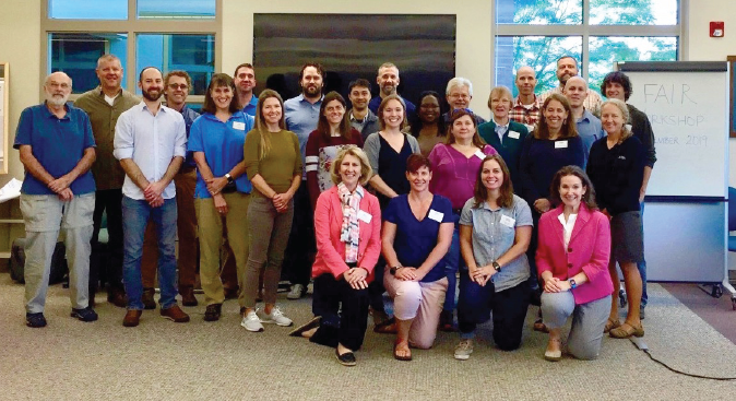 Figure 12. Twenty-six people smiling next to an easel holding a “FAIR Workshop September
                        2019” poster.