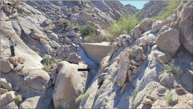 2.8. Narrow rocky valley with a small wall within the valley’s channel. A uniformed
                  person stands across from the wall.