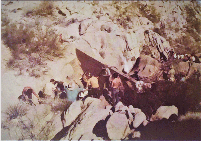 2.12. A group of people standing and sitting upstream of a retaining in a channell.
                  Rock is present almost to the base of the wall on the upstream side.