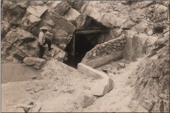 2.15. Mine-like entrance within a rock face framed by wooden beams with a wall separating
                  it from a small rectangular catchment.