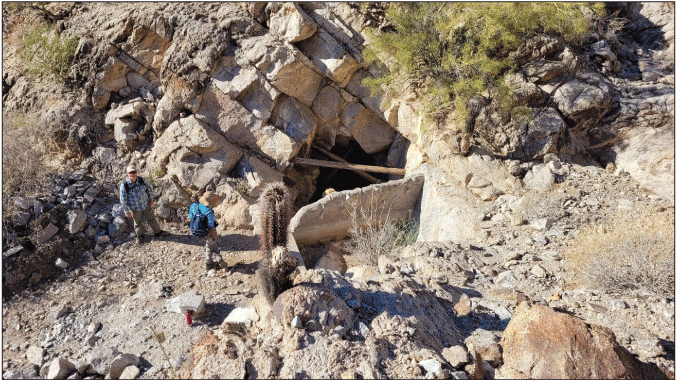 2.19. Tank entrance is dark inside with wooden beams and a rectangular catchment basin
                  separated by a short wall. Two people nearby are taller than the wall.