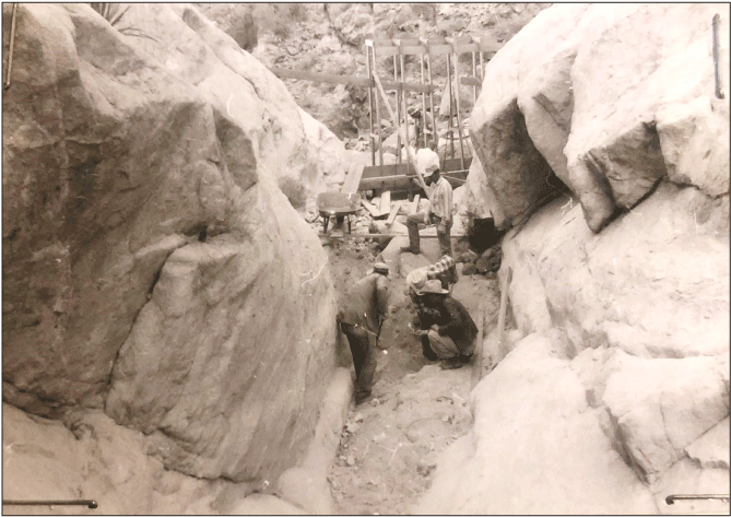 2.28. People working with equipment within a narrow channel bounded by rock.