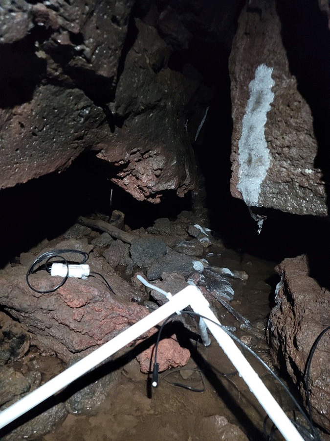 Equipment positioned above ice puddle on a reddish-brown rock surface. Ice is present
                  on some of the surrounding rock.