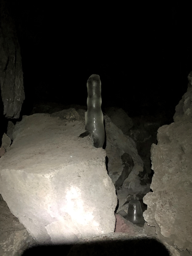 An ice stalagmite partially obscured by a section of rock.