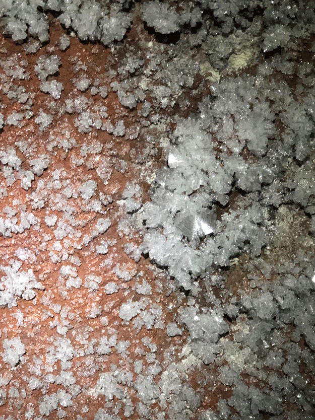 Large and small crystals of frost on a reddish cave wall.