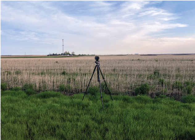 Spotting scope on a tripod stands in front of a cropland field with tall stubble.
