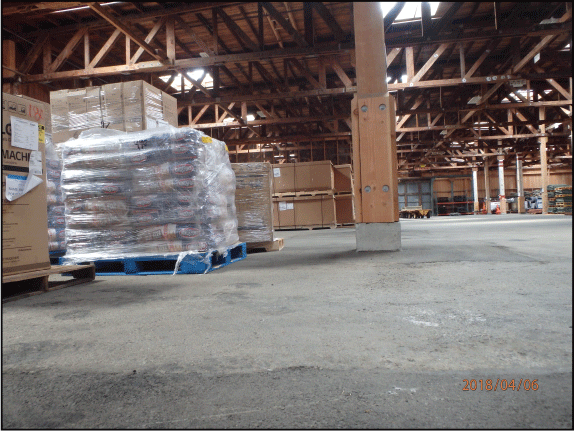 23. Wood scaffolding ceiling, wood walls, and asphalt floor of Warehouse 1, with several
pallets of cargo stored inside.