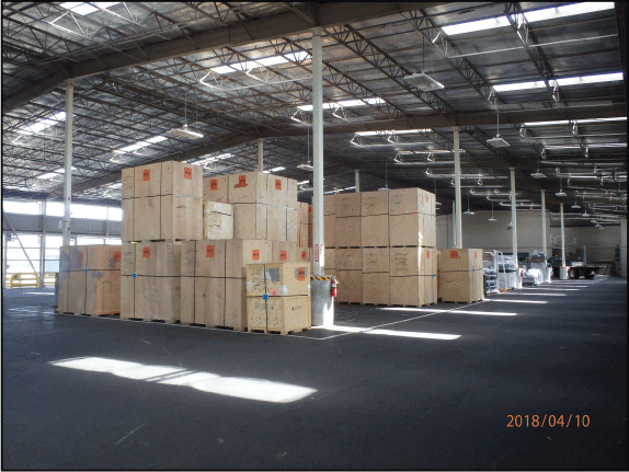 26. Wood-crates stacked on wood pallets inside Warehouse 2, which has a high steel-raftered
ceiling, asphalt floor, and open link doors.