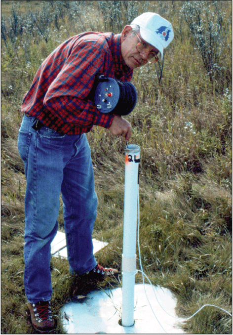 Man standing in grassy area holding measure equipment.