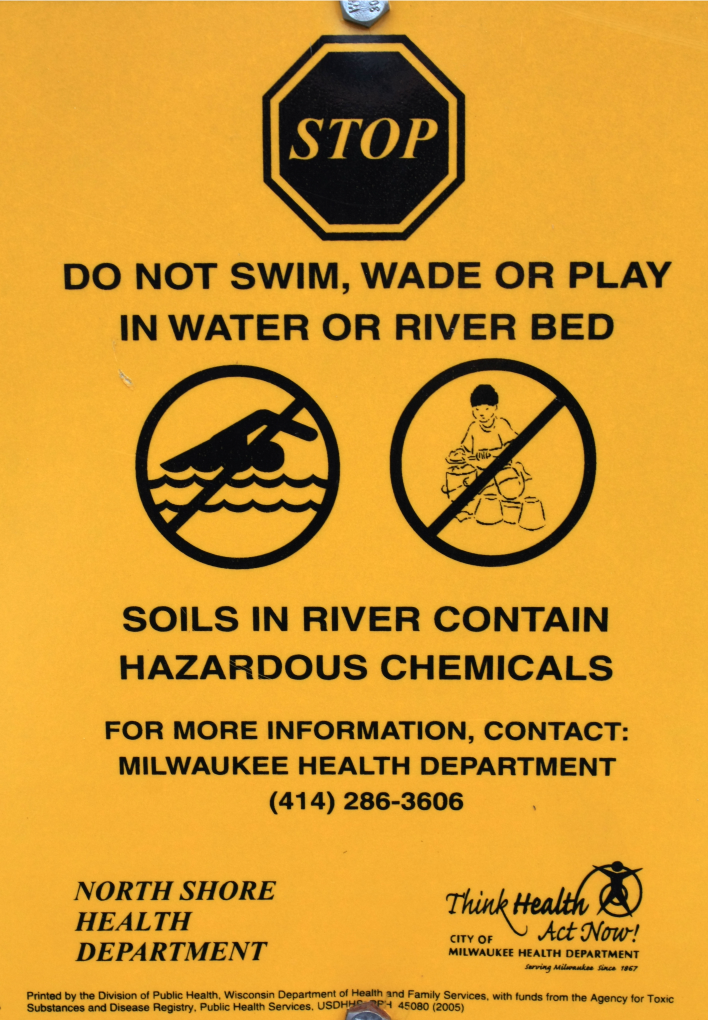 Sign saying do not swim, wade or play in water because of hazardous chemicals.