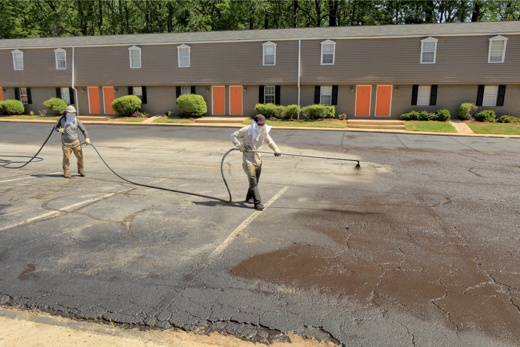Photograph of two workers with a hose and sprayer applying a seal coating chemical
                              to an asphalt parking lot.