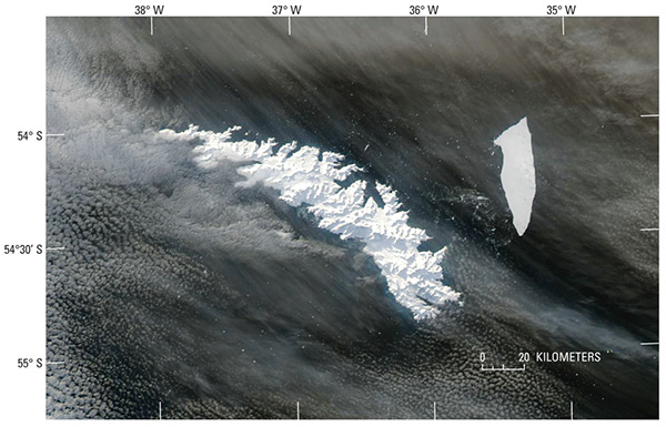 Figure 16.—MODerate-resolution Imaging Spectroradiometer (MODIS) image of South Georgia Island on 15 July 2004. The island is completely covered with snow, masking the 43 percent of the island not covered with glaciers (see fig. 17). The A-38B tabular iceberg and associated smaller icebergs can be seen east of the island. The “parent” A-38 iceberg (140 km long, 40 km wide; Ferrigno and others, 2005) calved from the Ronne Ice Shelf, East-Antarctica in early October 1998, before breaking into two tabular icebergs (A-38A and A-38B) on 22 October 1998 (Ferrigno and others, 2005). During the 6-year interval between the initial calving event and the date of this MODIS image, the A-38B iceberg has been reduced from its original dimension to about 60 km long, 15 km wide. MODIS image from the Terra satellite of the National Aeronautics and Space Administration. NASA Terra MODIS image at http://veimages.gsfc.nasa.gov/6835/SouthGeorgia.A2004197.1635.250m.jpg.