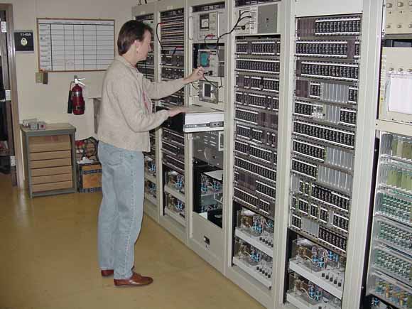 photograph of scientist standing in front of her rack of electronic equipment