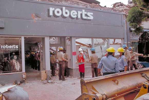 workers with dust masks clearing out store; bulldozer in foreground