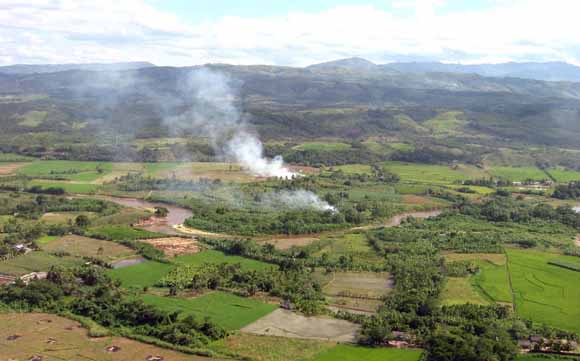 photo taken from low-flying aircraft of fields, forested land, and two smoke plumes