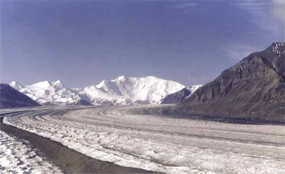 photo of snow-covered mountains in background, and large glacier flowing into the foreground