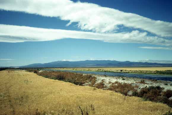 Photo of grasslands with stream in foreground and volcanic features along the skyline