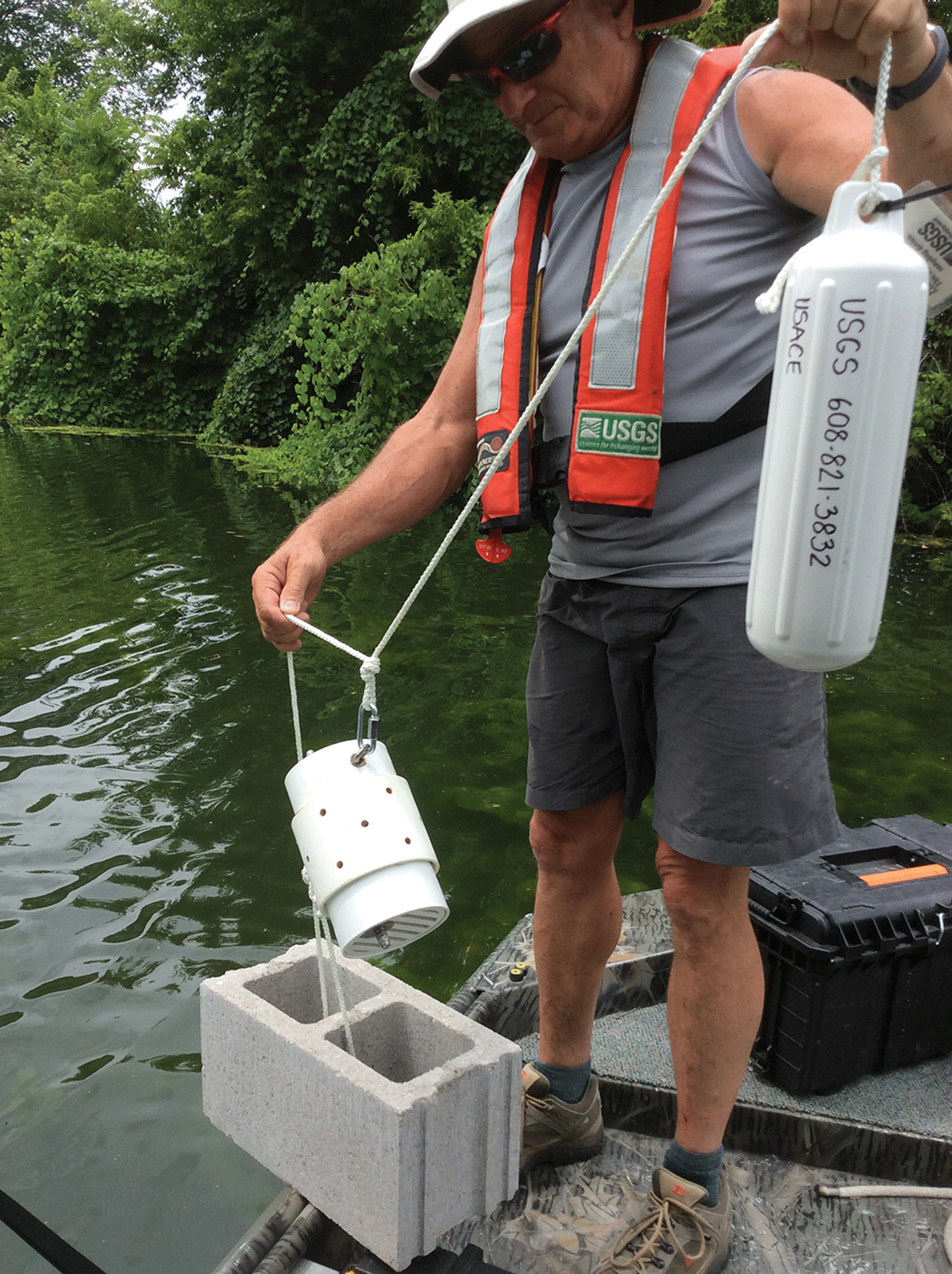 Man standing on a dock over water holding the sampler attached to a cement block.