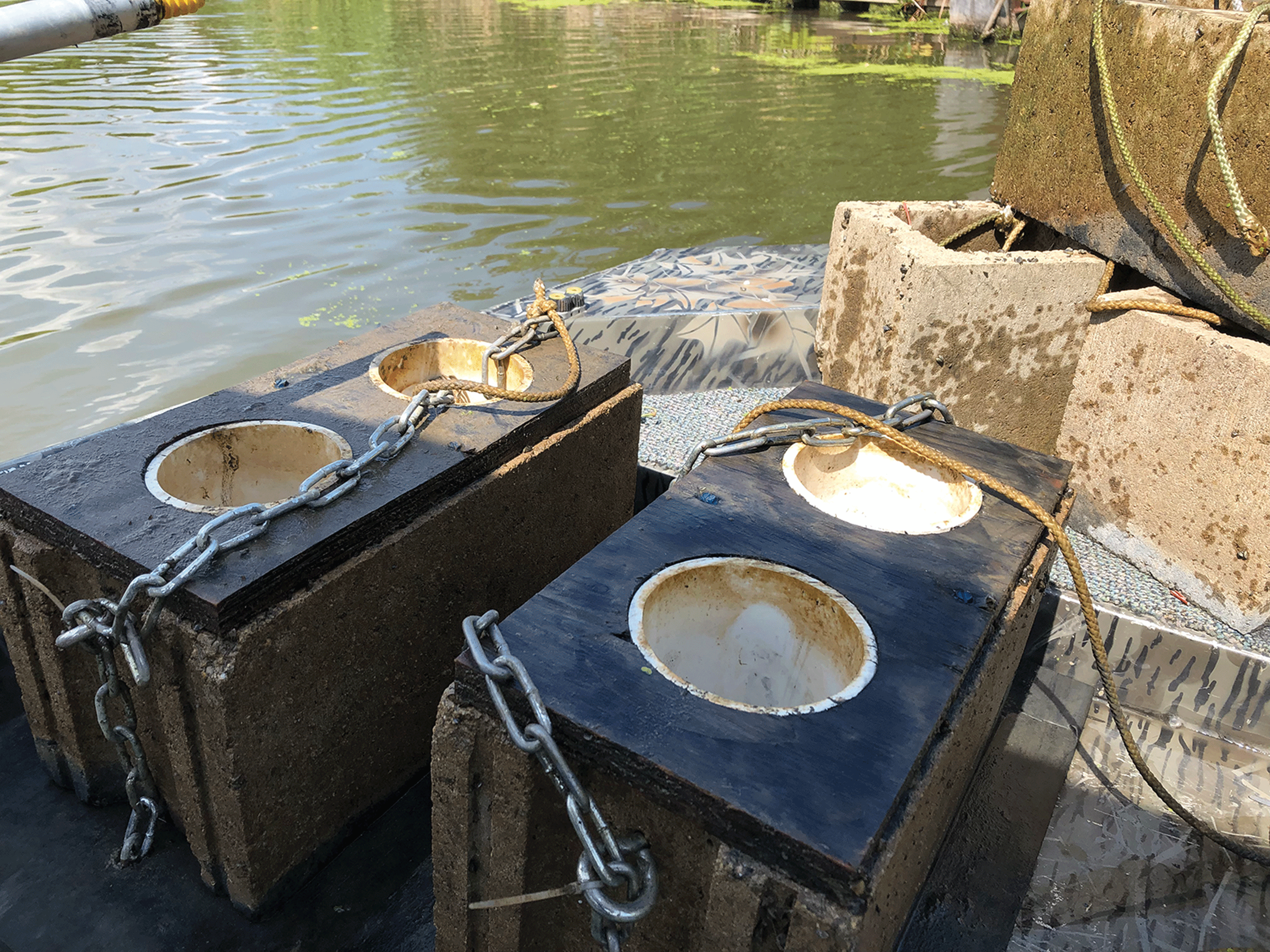 Two samplers sitting on a dock over water. The samplers are in large cement blocks
                        with chains attached.