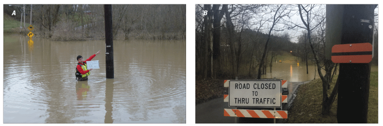 Person almost waist deep in water points to a high-water mark, above head level, on
               a telephone pole; road is closed where the road and the land beside it are flooded.