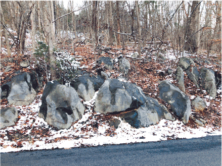 Groups of boulders sit near each other in the partially snow-covered wooded area.