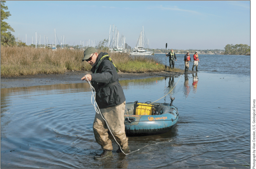 People in water removing yellow cable from rubber raft.