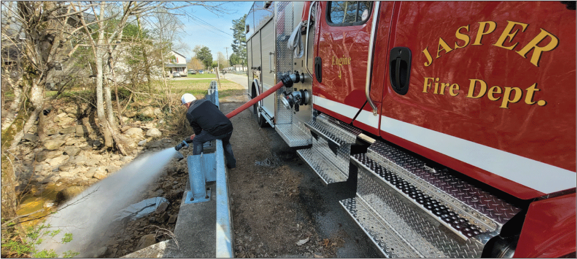 Alt text: Personnel holding fire hose discharging water into stream channel.