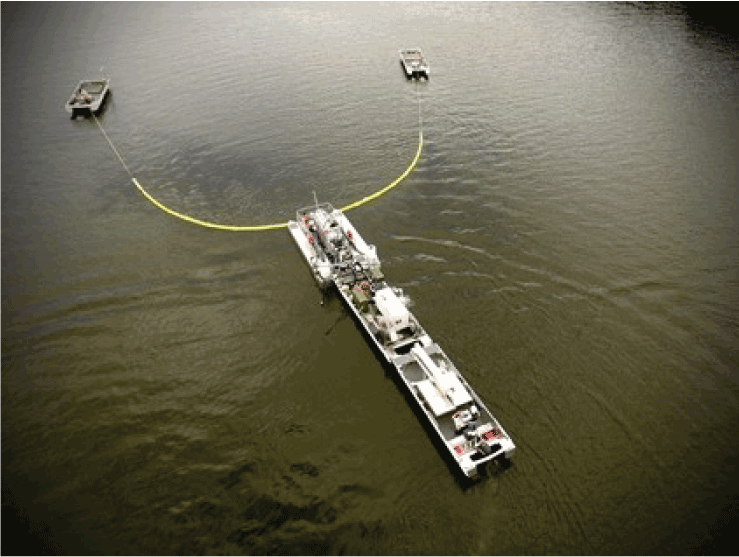 Two small boats in front of and connected to a barge are on a lake; the dark water
                     has small ripples.