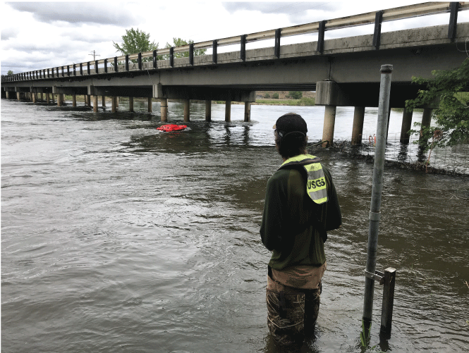 Photograph showing a U.S. Geological Survey (USGS) hydrologic technician maneuvering
                        a remote-controlled boat with an acoustic Doppler current profiler into position to
                        verify the accuracy of two sonar devices at Idaho Transportation Department bridge
                        structure number 19935. Site is co-located with USGS station Payette River near Letha,
                        Idaho (USGS station number 13250000)