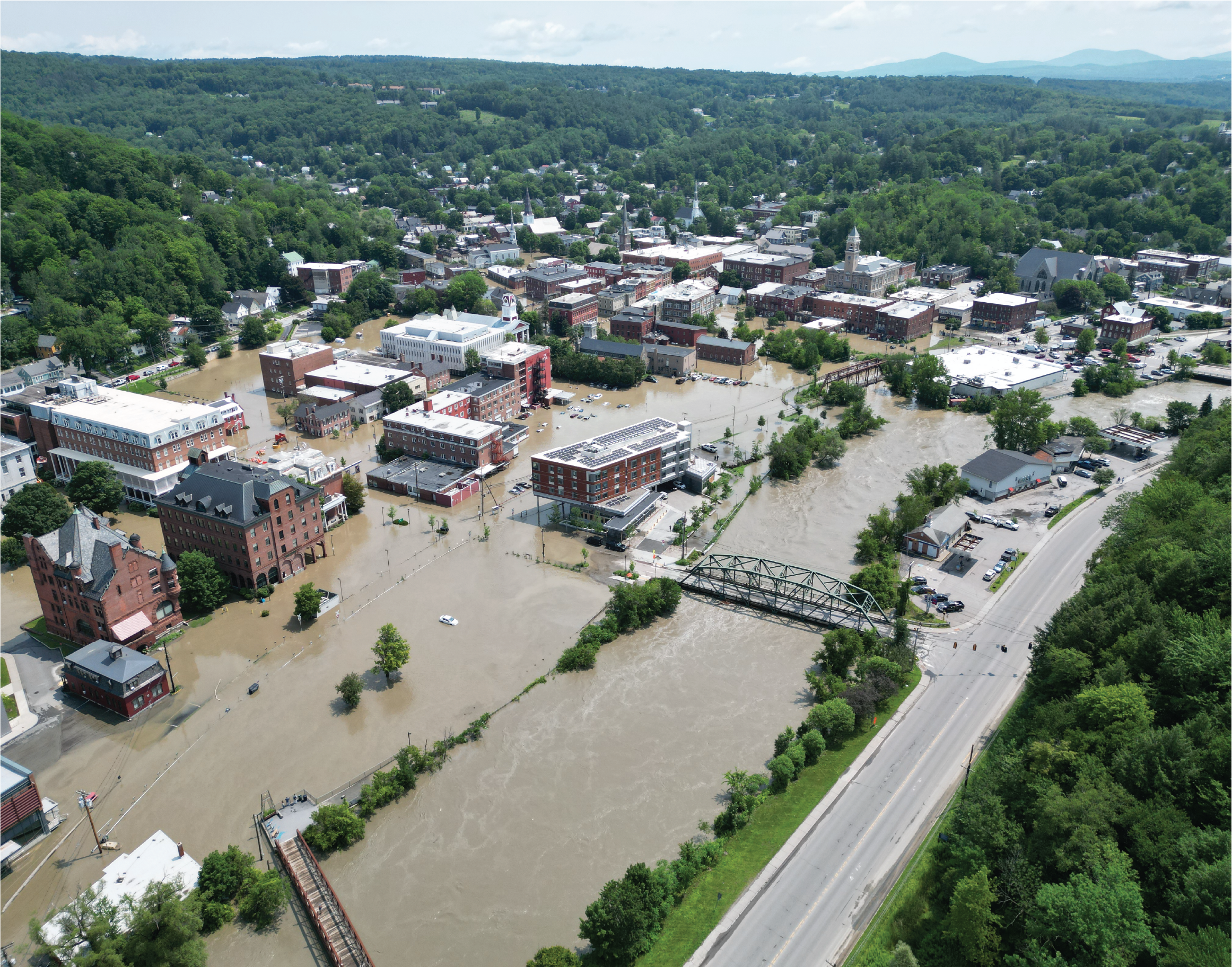 Arial image of flooding in a city, with floodwaters overtaking cars and buildings.