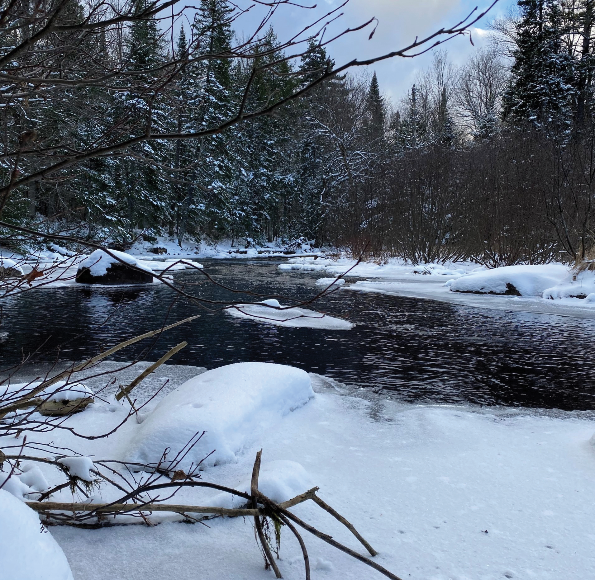 Photograph showing the Chubb River in winter with patches of ice on the water and
snow on the tree-lined banks.
