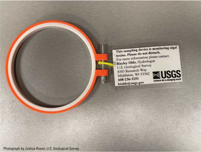 6. An example identification tag is attached to the SPATT sampler hoop with a zip
                        tie and contains the message “This sampling device is monitoring algal toxins. Please
                        do not disturb,” followed by the contact information of the lead researcher and the
                        U.S. Geological Survey (USGS) logo.