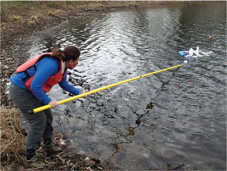 Sampling with a long pole and bottle near water-quality instrumentation.