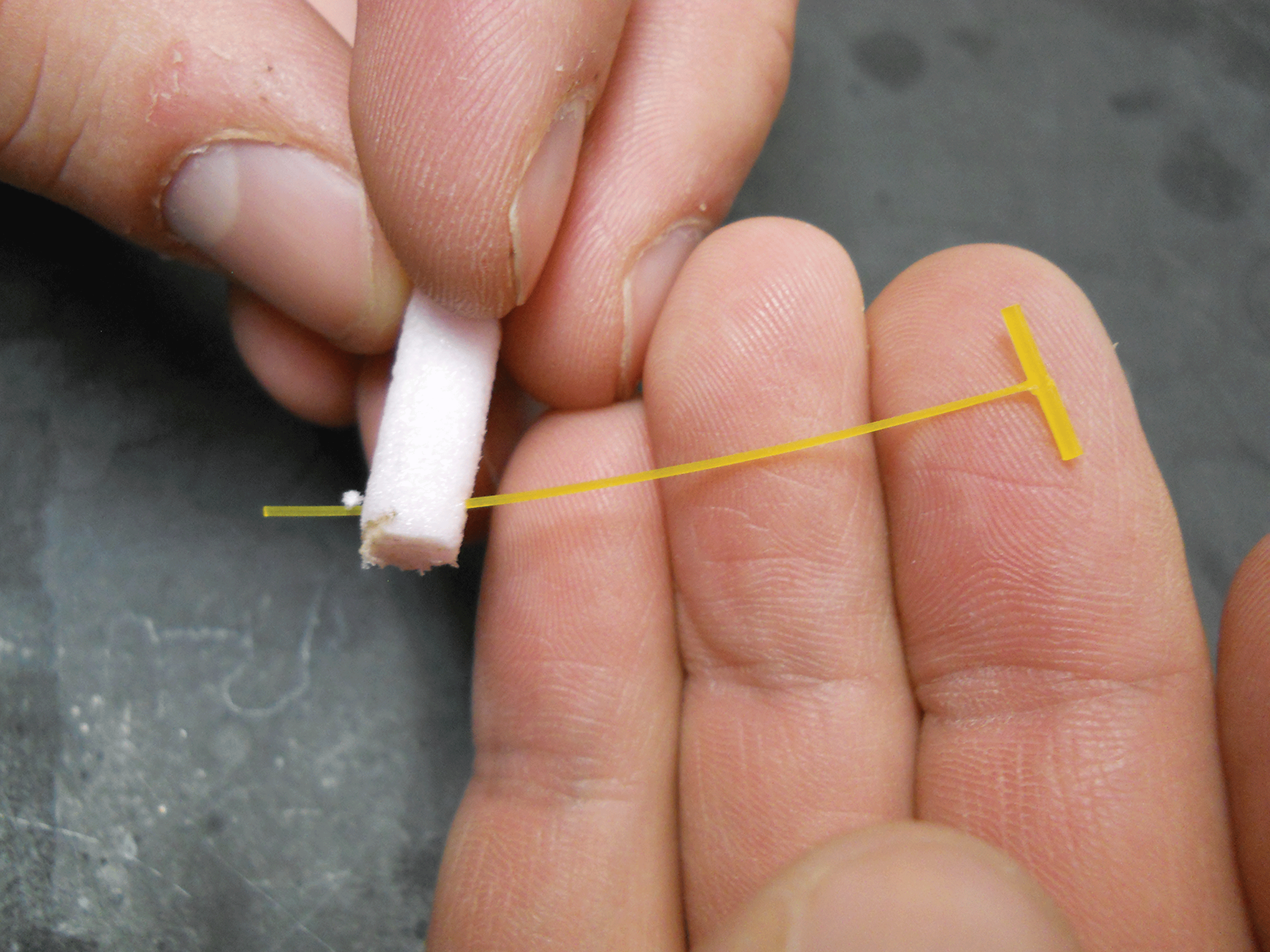 Photograph showing a T-bar tag being inserted perpendicular through the end of pink
                        foam.