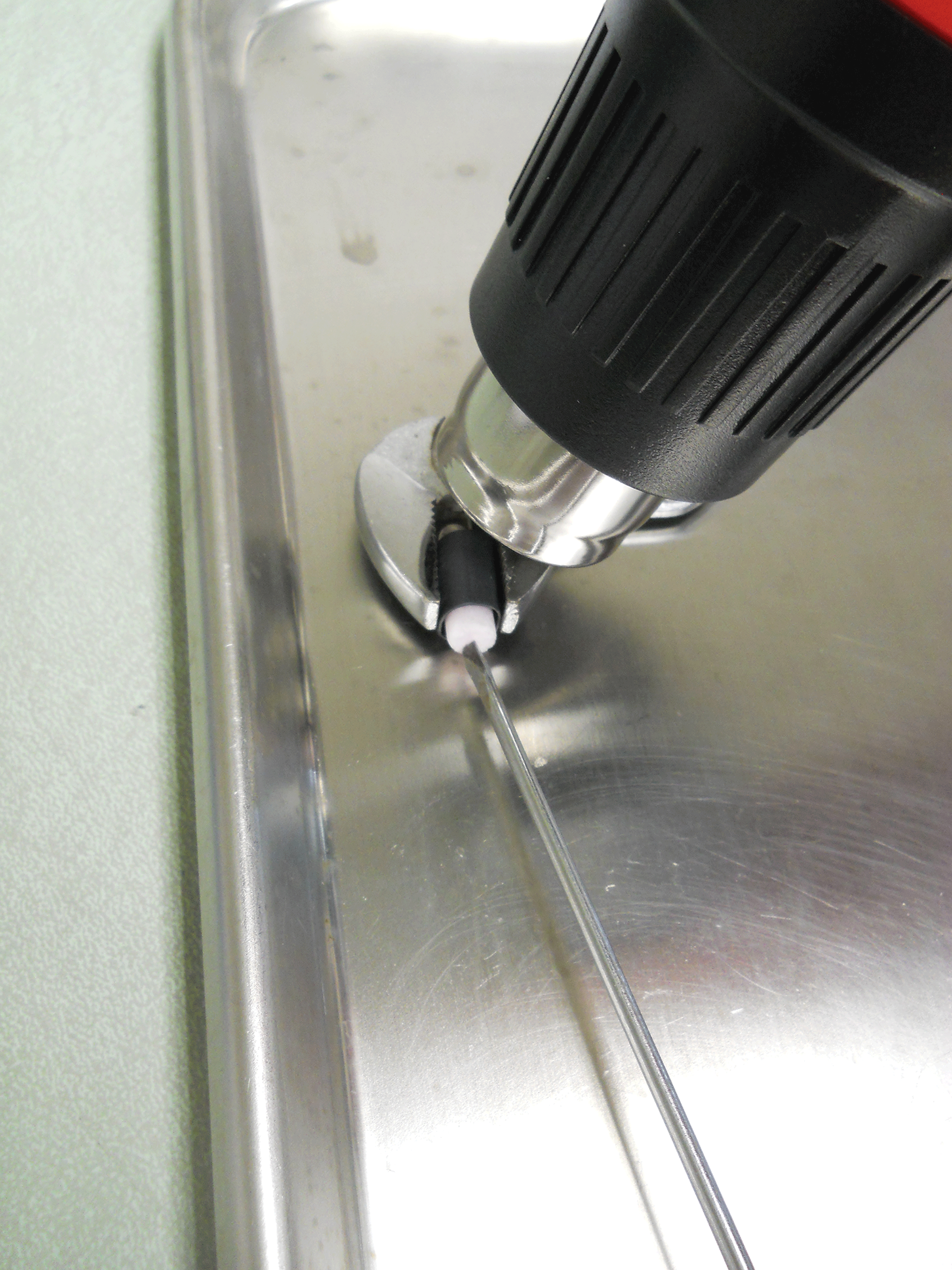 Photograph showing pliers being used to hold tag assembly while shrink tubing is heated.