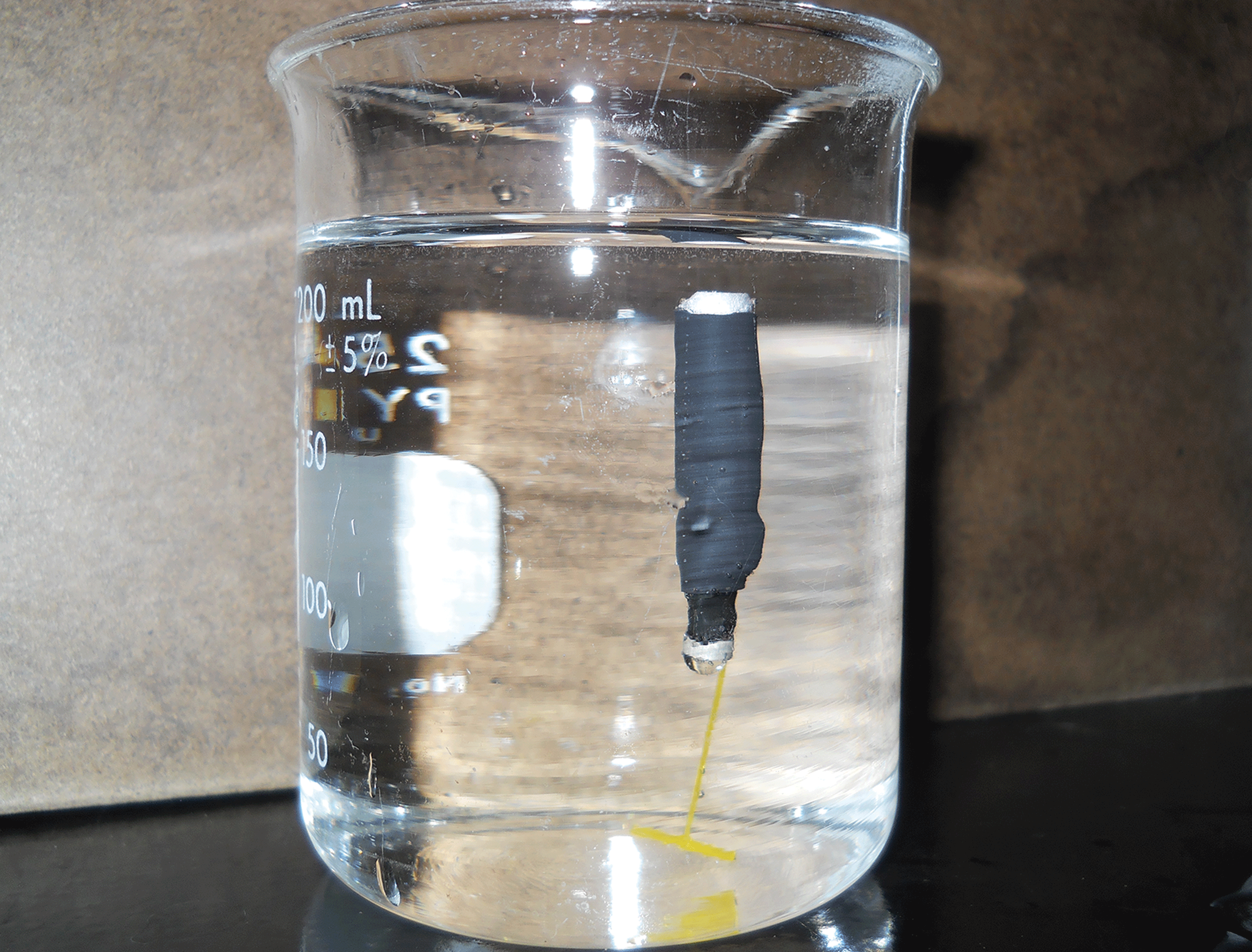 Photograph shows a neutrally buoyant external acoustic transmitter attachment device
                        upright in a beaker full of water.