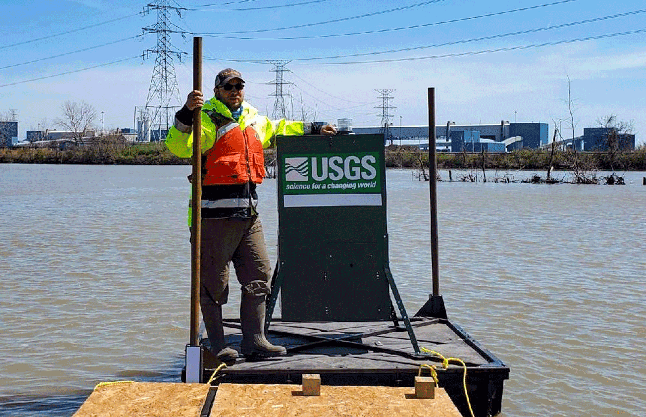 A biologist stands on a fully constructed bait delivery platform floating on water.