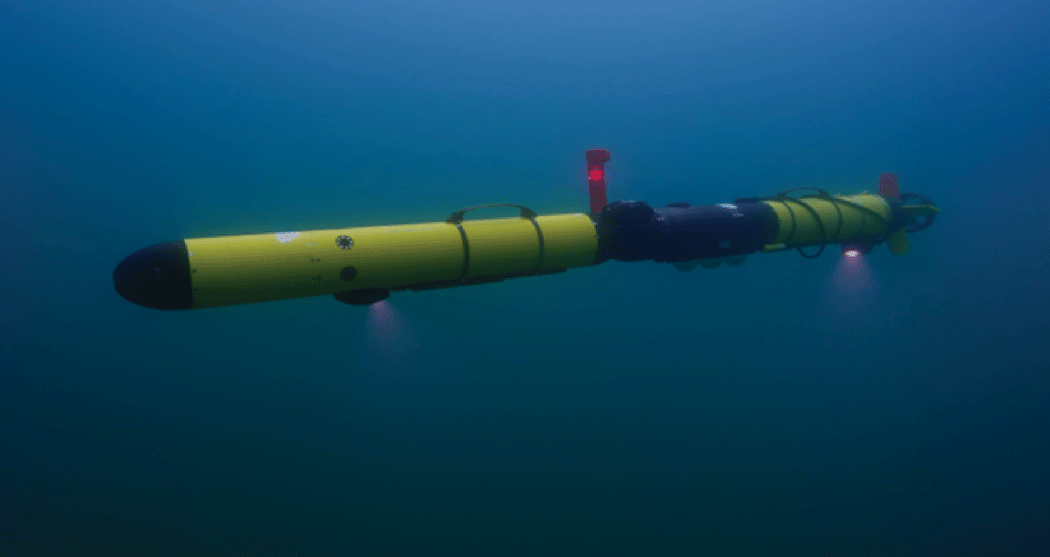 A yellow and black cylindrical robot with forward and aft lights shining downward
in clear, deep blue water.